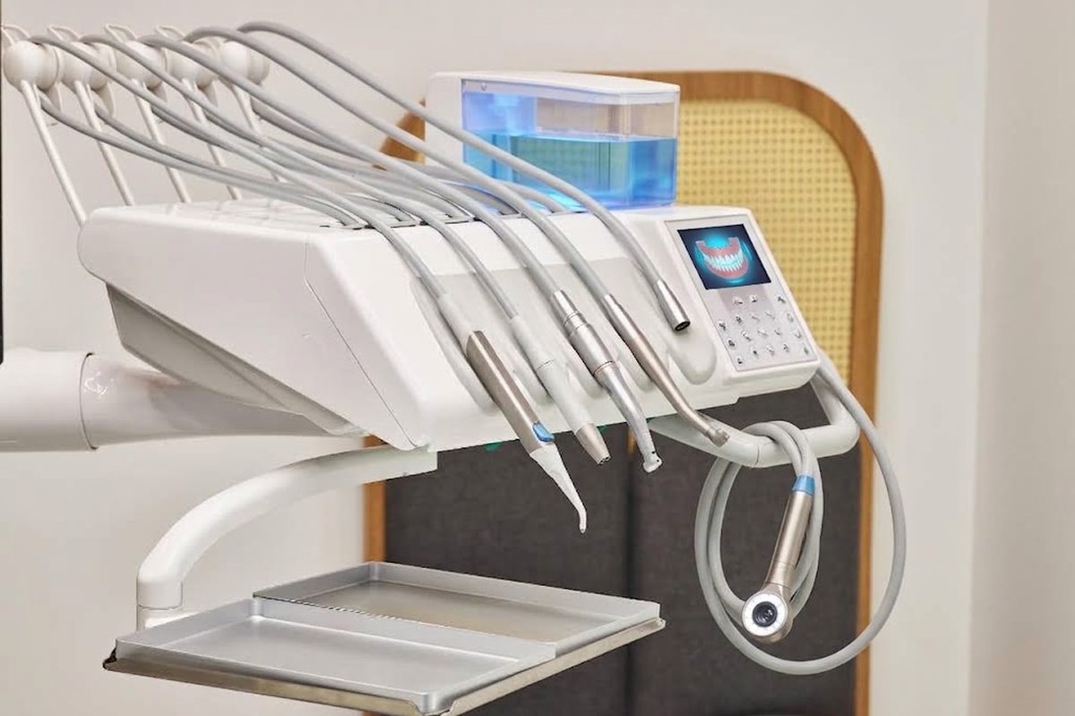 A dental delivery unit: handpieces, three-in-one syringe and curing light on their holders beside the chair